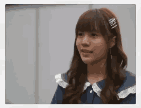 a young girl with long hair and a hair clip in her hair is looking at the camera .