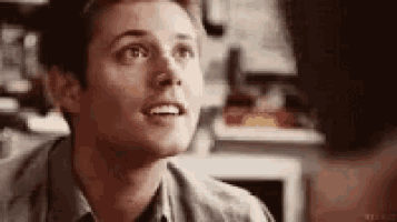 a man is smiling and looking up at another man in a room .