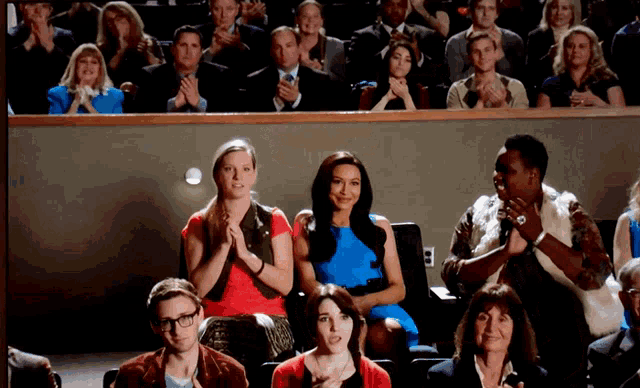 a woman in a blue dress sits in a crowd of people clapping