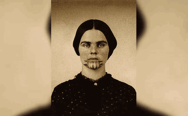 a woman with a tattoo on her face is standing in front of a white background .