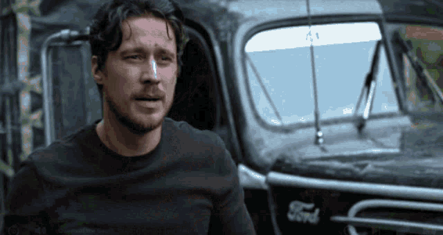 a man in a black shirt stands in front of a black ford truck