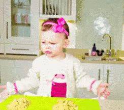 a little girl with a pink bow on her head is sitting at a table with food