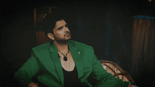 a man wearing a green jacket and a black tank top is sitting in a chair