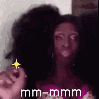 a woman with a wig on her head is making a funny face and says mm-mmm .