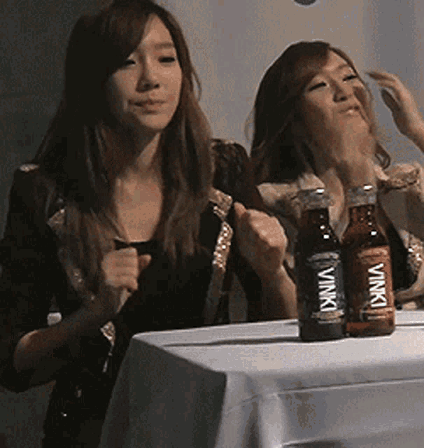 two women sitting at a table with two bottles of vinki