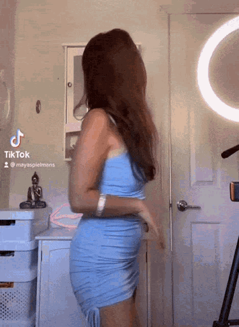 a woman in a light blue dress is dancing in front of a ring light and a buddha statue