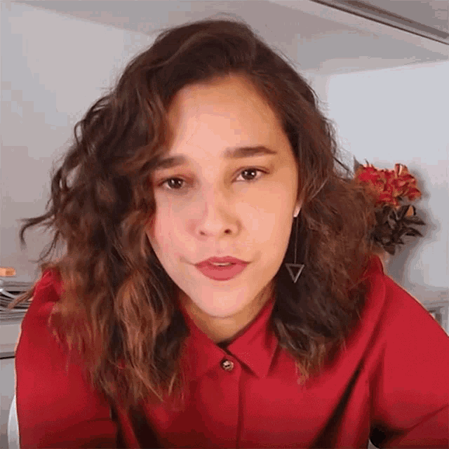 a woman wearing a red shirt has a triangle shaped earring on her left ear