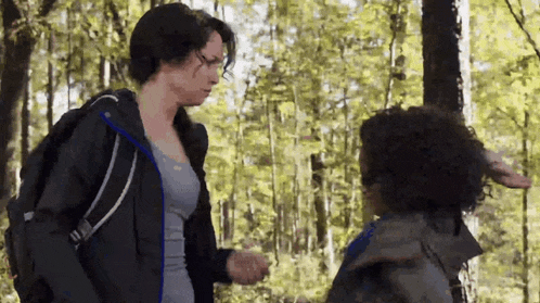 a woman with a backpack is standing next to a boy in the woods .