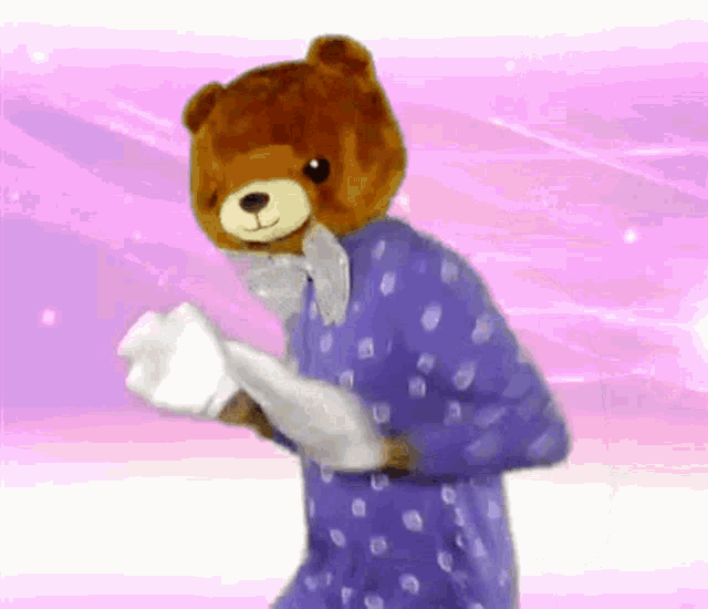 a teddy bear wearing a polka dot pajama top is holding a piece of paper