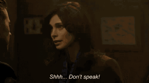 a woman is talking to a man in a dark room and says `` shhh ... don 't speak '' .