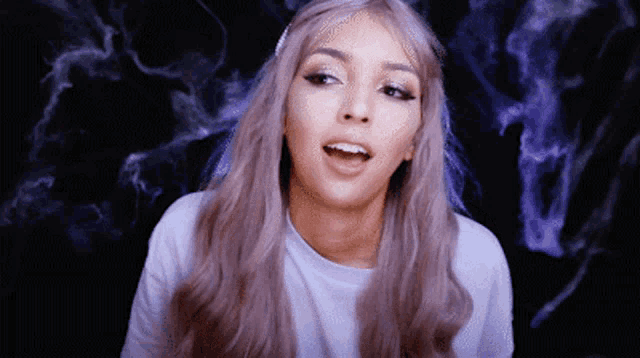 a woman with purple hair is wearing a white shirt and making a funny face