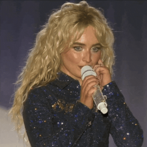 a blonde woman singing into a microphone in a blue shirt