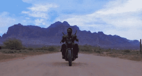 a man is riding a motorcycle on a dirt road with mountains in the background