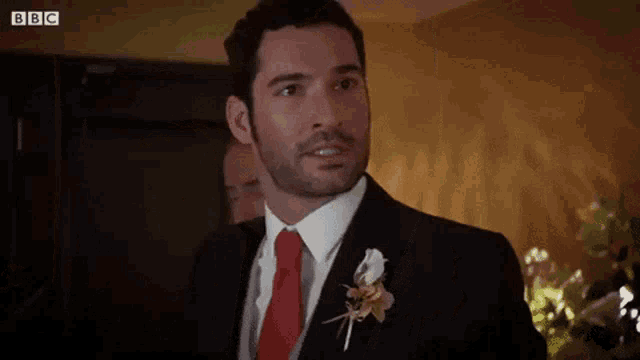 a man in a suit and tie with a flower in his lapel is standing in a room .