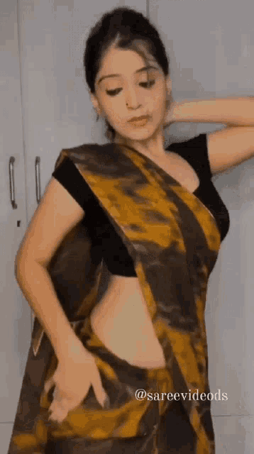 a woman in a crop top and a saree is standing in front of a closet .