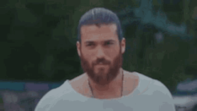 a man with a beard and long hair is wearing a white shirt and necklace .