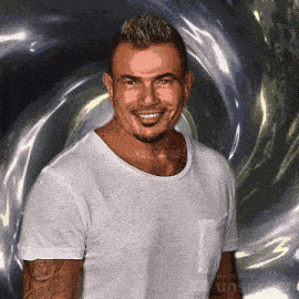 a man in a white t-shirt is smiling in front of a shiny background