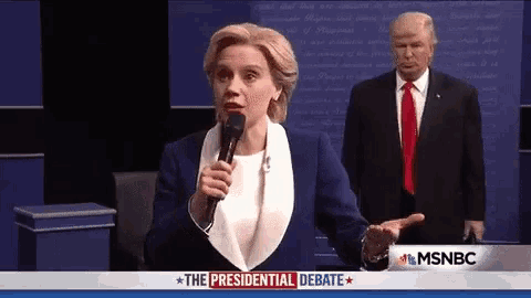 a woman is speaking into a microphone while a man in a suit and tie stands behind her