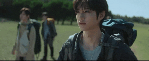 a man with a backpack is walking in a field with two other men .