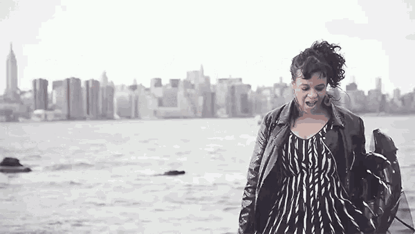 a woman in a striped dress is standing in front of a body of water with a city in the background .