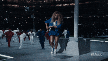 a woman in a blue dress is dancing in front of an apple music halftime show sign