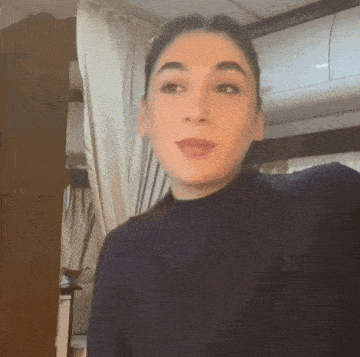 a woman wearing a blue sweater is standing in front of a white curtain .