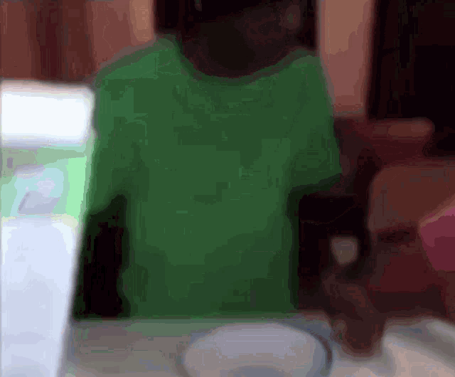a person in a green shirt is sitting at a table with a bowl