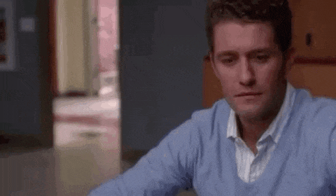 a man in a blue sweater is sitting at a table in a room .
