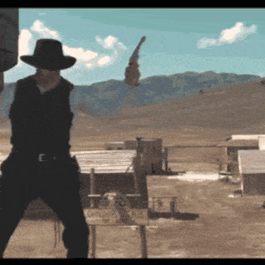 a man in a cowboy hat is holding a gun in front of a sign that says condor ranch