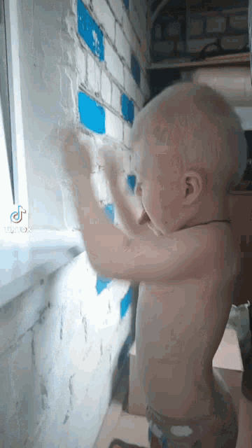 a shirtless child is standing next to a brick wall