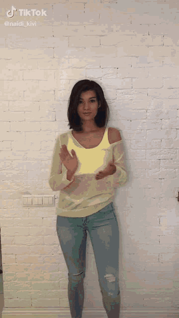 a woman standing in front of a white brick wall with tiktok written on the bottom of the screen