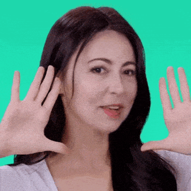a woman with long dark hair is making a funny face with her hands .