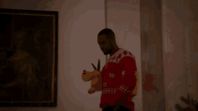 a man in a red sweater is holding a stuffed reindeer in front of a painting