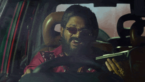 a man with a beard is driving a car and holding a piece of paper that says ' e ' on it