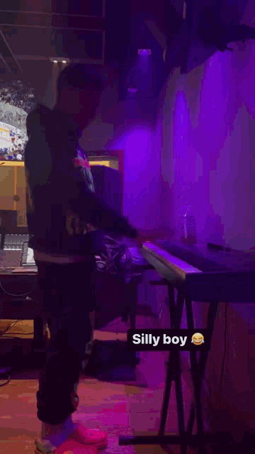 a man in a hoodie is standing in front of a keyboard in a room with purple lights .