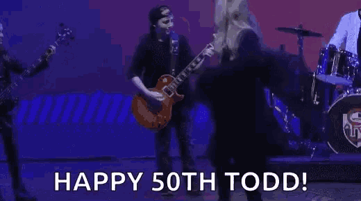 a man is playing a guitar and a woman is dancing on a stage in front of a drum set .