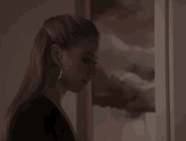 a woman wearing hoop earrings stands in front of a framed picture