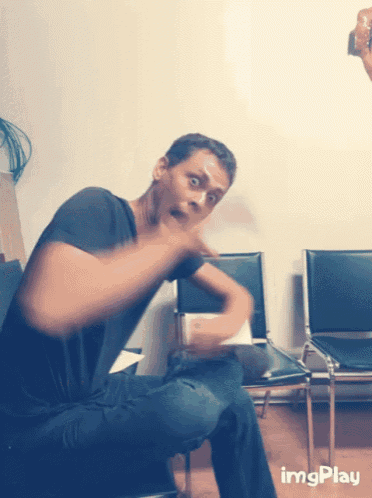 a man sitting in a chair with a surprised look on his face and the words imgplay on the bottom right