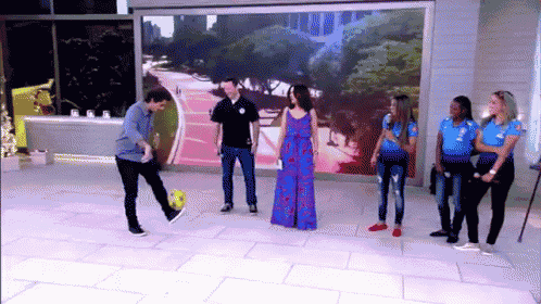 a man kicking a soccer ball in front of a group of women