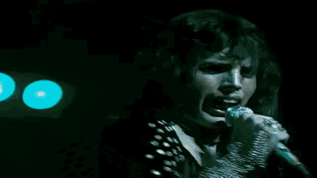 a man is singing into a microphone on a stage in front of a green light .