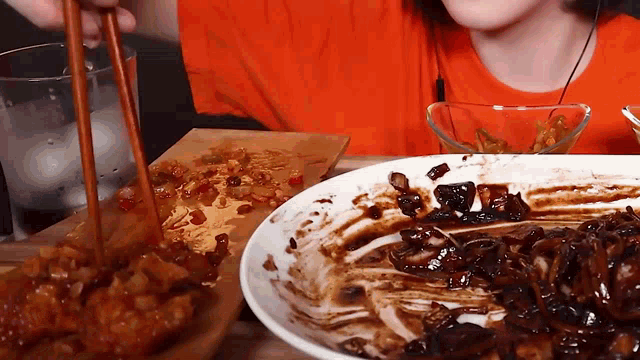 a person eating food with chopsticks next to a plate of food .