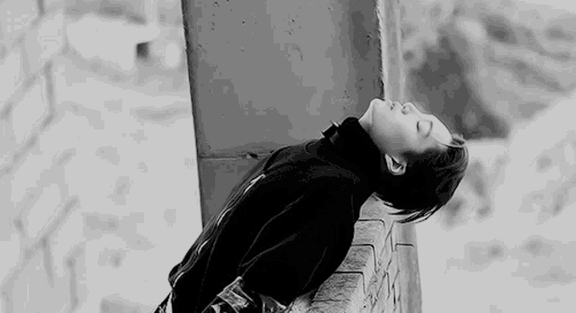 a black and white photo of a person leaning against a wall with their head down .