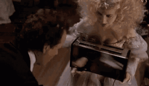 a man is standing next to a woman in a white dress holding a toaster oven .