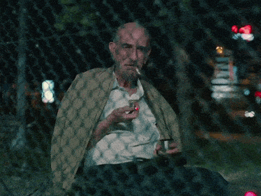 a man smoking a cigarette behind a chain link fence at night