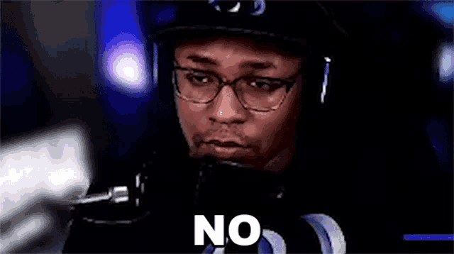 a man wearing glasses and headphones is sitting in front of a microphone and saying `` no '' .