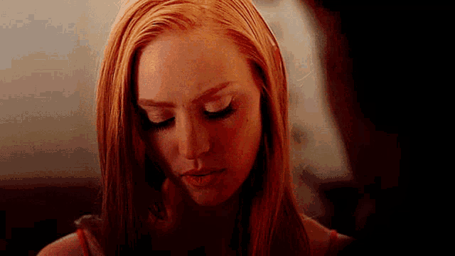a close up of a woman 's face with red hair looking down .