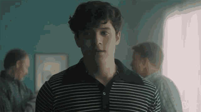 a man in a striped shirt is standing in a room with other men behind him .