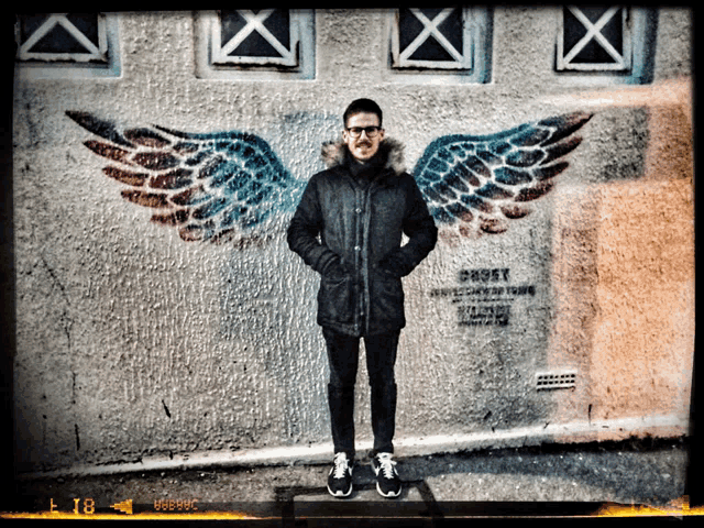 a man stands in front of a wall with wings painted on it and the number 18 on the bottom