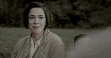 a woman in a plaid jacket is sitting in a field looking at the camera .