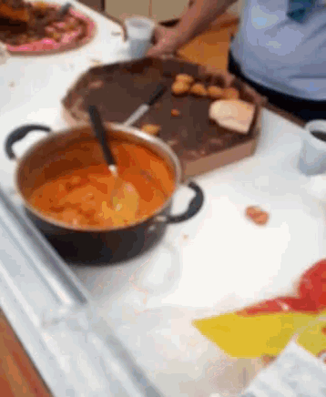 a pot of sauce with a spoon in it sits on a counter next to a pizza box